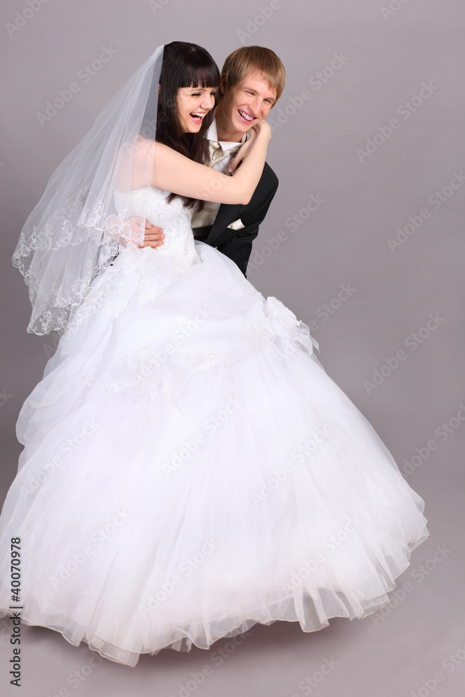 Laugh groom downs on floor beautiful bride in studio on gray Laugh groom downs on floor beautiful bride in studio on gray