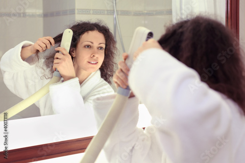 Smiling woman dressed in white bathrobe stands near mirror