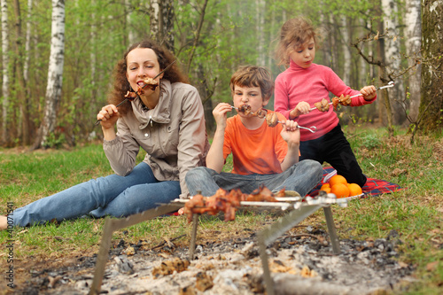 Mother and her children eat grilled shish kebab outdoor