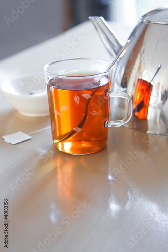 Glass mug with tea, teapot en teabag on table photo
