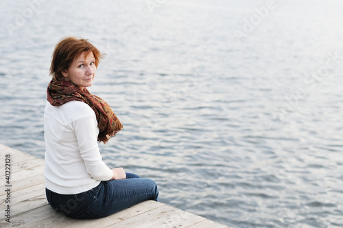 Middle age woman sitting on wood boards by the water