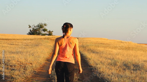 Girl walking on empty rural road far away in summer day