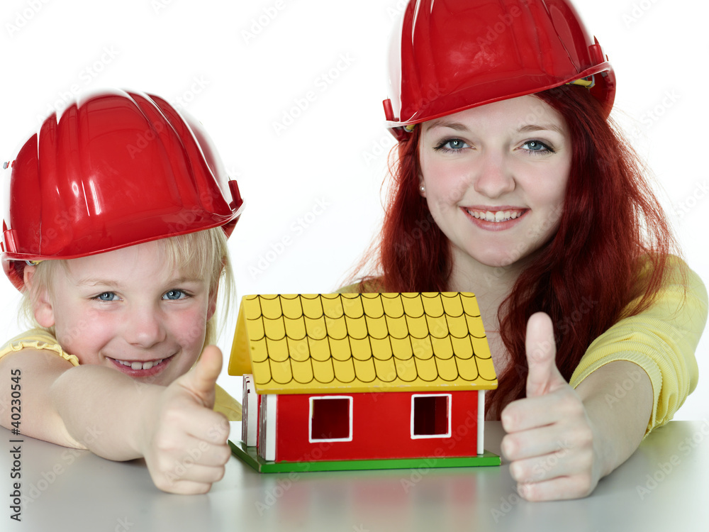 Two girls with helmet show thumb up for building a house Two girls with helmet show thumb up for building a house