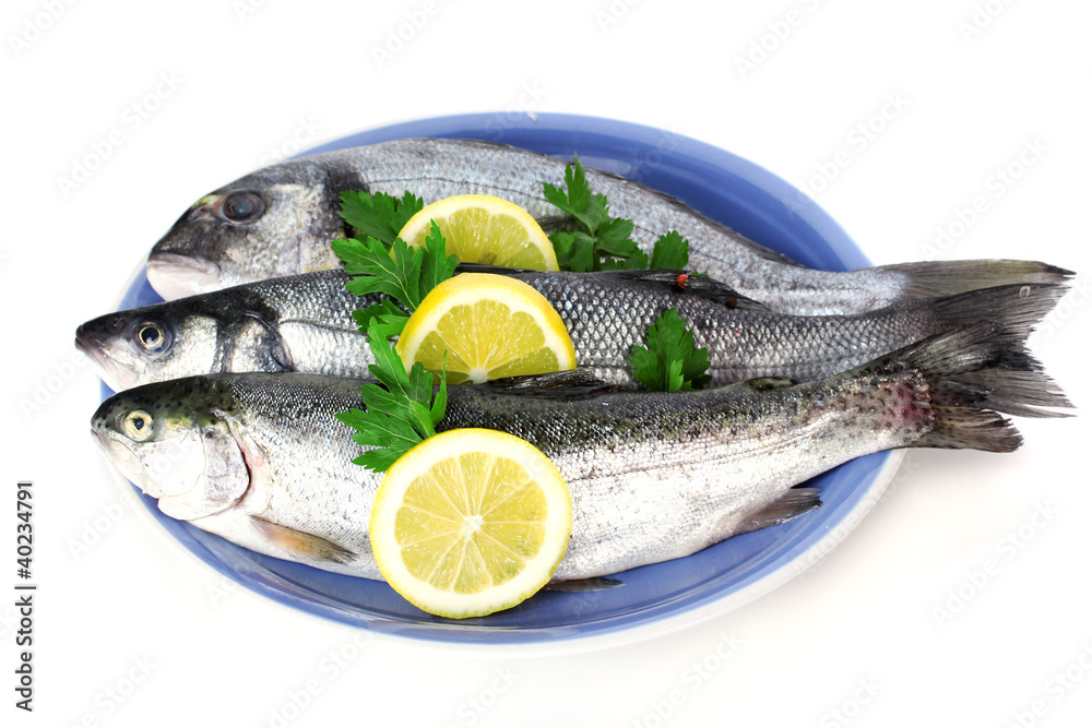 Fresh fishes with lemon and parsley on plate isolated on white Fresh fishes with lemon and parsley on plate isolated on white