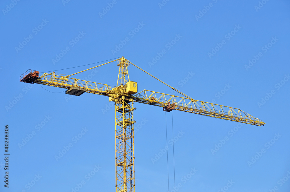 Yellow construction tower crane against blue sky