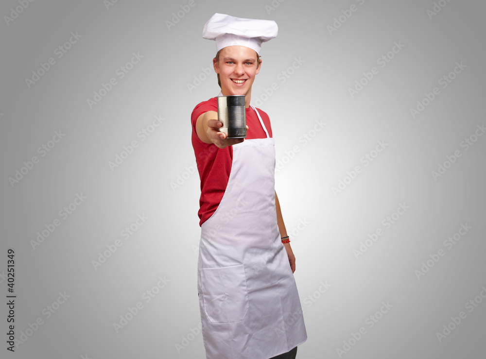 portrait of young cook man holding a metal tin can over grey bac portrait of young cook man holding a metal tin can over grey bac