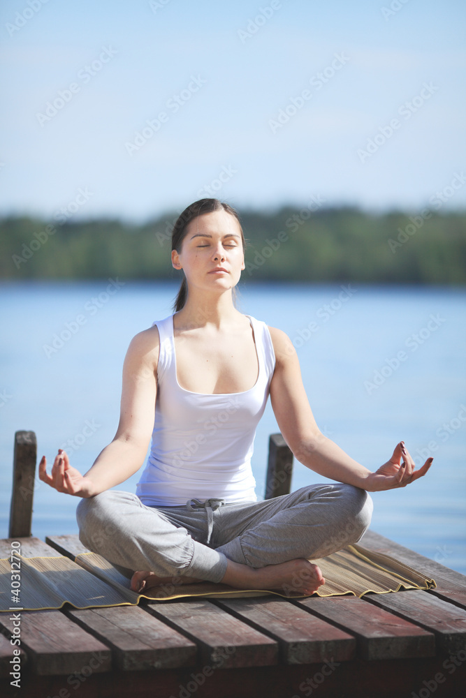 beautiful young girl training yoga near a lake