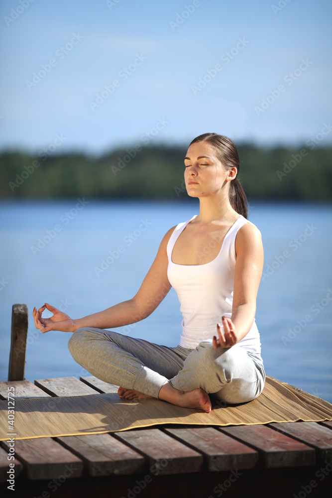 beautiful young girl training yoga near a lake