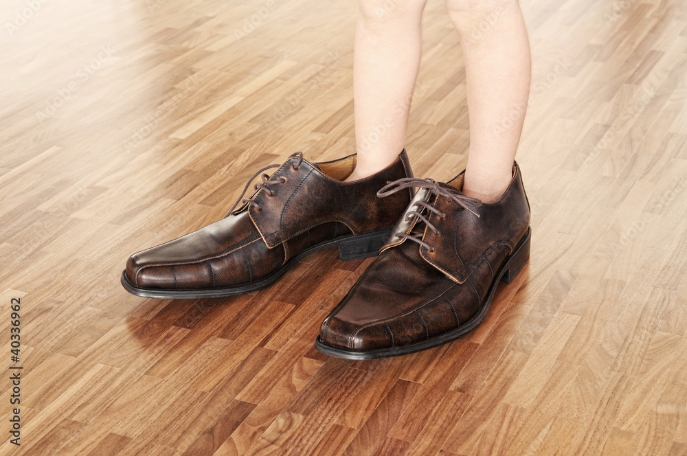 Toddler wearing adult shoes on walnut parquet floor.