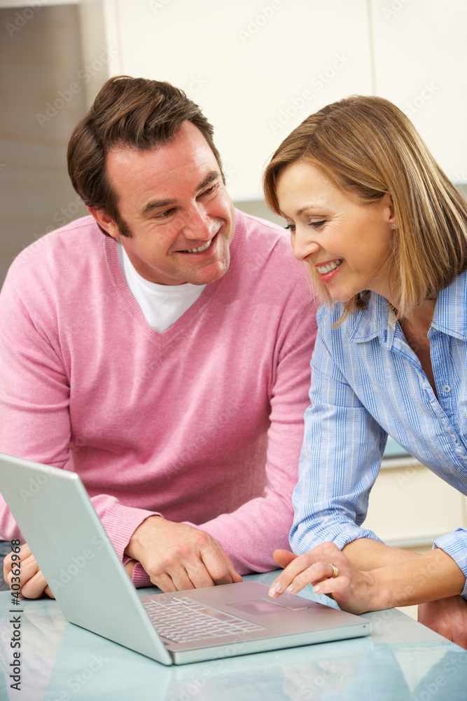 Mature couple using laptop in domestic kitchen Mature couple using laptop in domestic kitchen