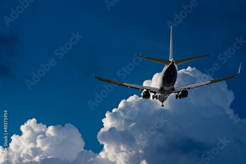 Passenger jet landing against a blue sky with white fluffy cloud