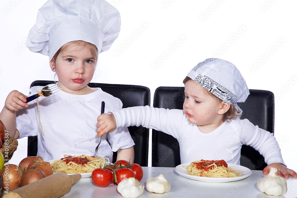 Zwei Mädchen mit Kochmütze essen Spaghetti Porträt Zwei Mädchen mit Kochmütze essen Spaghetti Porträt