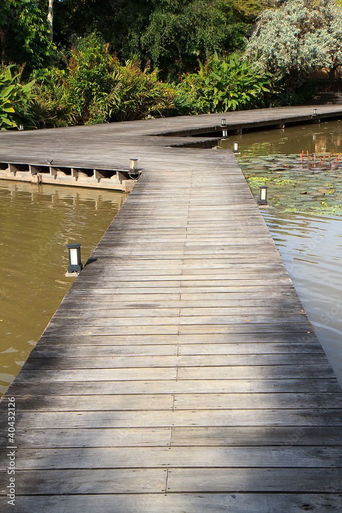 a wooden plank boardwalk on the pond to summerhouse in a garden a wooden plank boardwalk on the pond to summerhouse in a garden