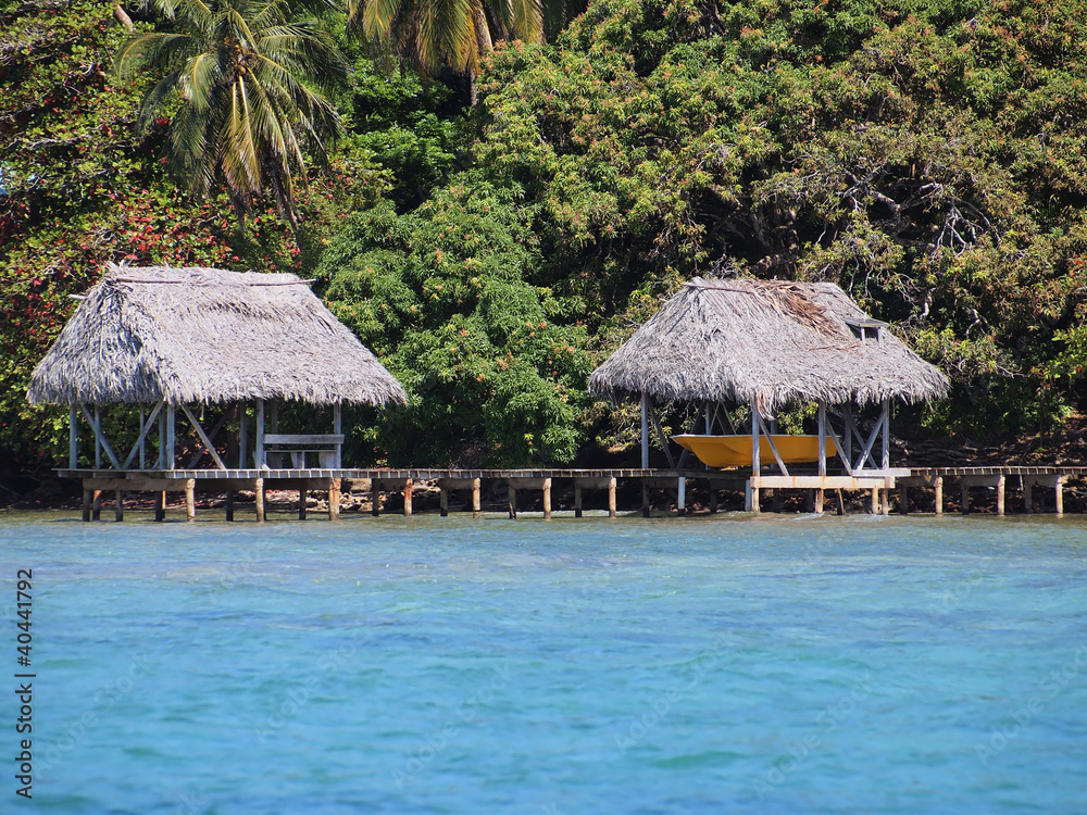 A boathouse and palapa on stilts over the sea with lush tropical vegetation in background