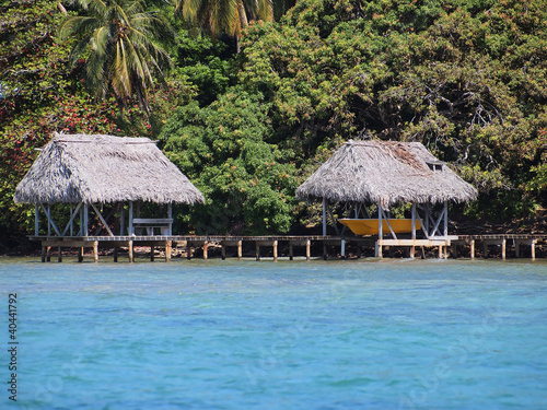 A boathouse and palapa on stilts over the sea with lush tropical vegetation in background