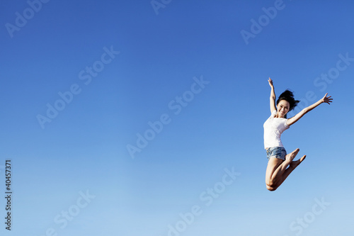 Joyful woman jumping over clear blue sky
