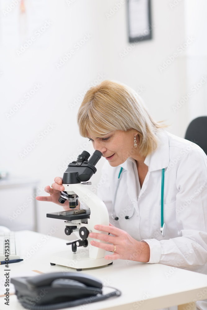 Middle age female researcher looking in microscope Middle age female researcher looking in microscope