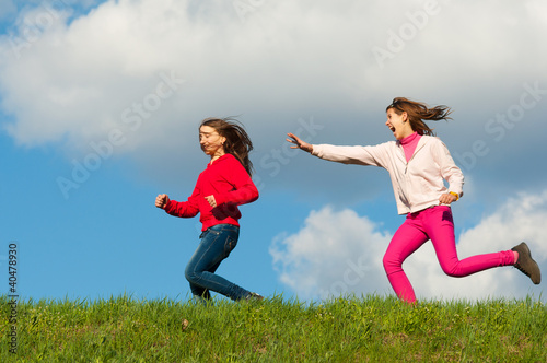 Two happy teenage girls running on the meadow