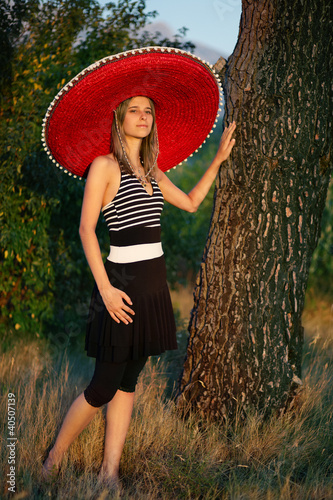 Young girl with a sombrero leaning on a tree © linkova