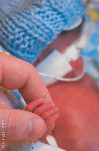 A premature baby holds his father's finger photo