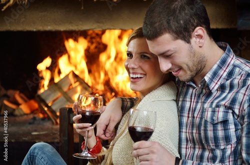 Young romantic couple sitting on sofa in front of fireplace at h photo