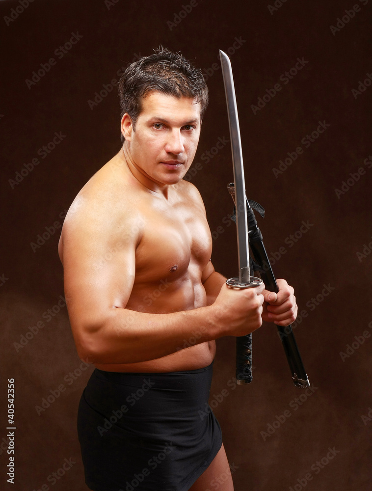 A muscled male posing with a sword on brown background A muscled male posing with a sword on brown background