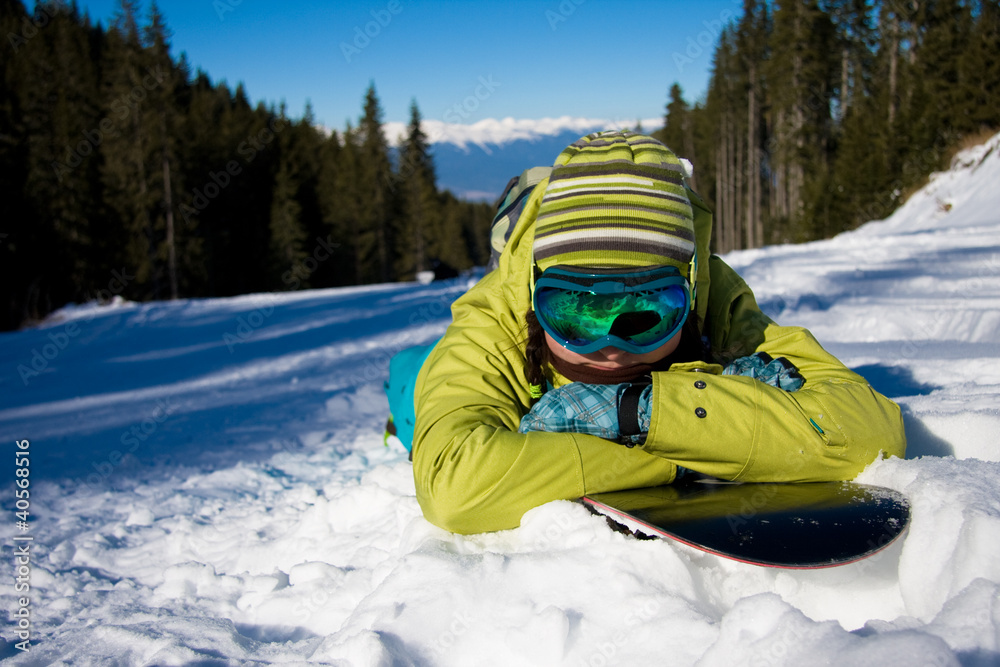 Girl lying on snowboard against forest and slope Girl lying on snowboard against forest and slope