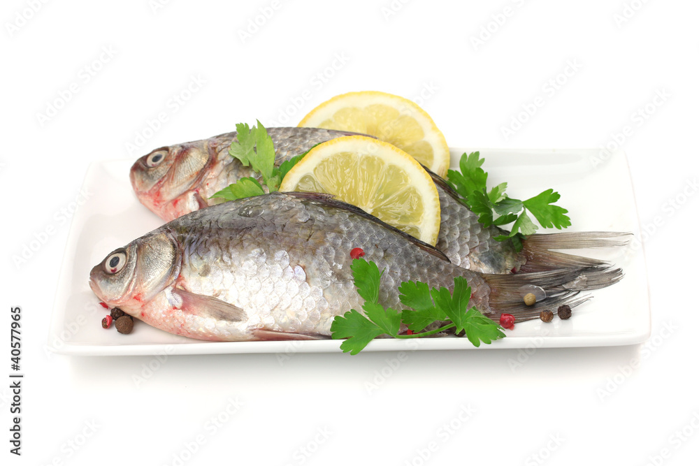Fresh fishes with lemon and parsley on plate isolated on white Fresh fishes with lemon and parsley on plate isolated on white