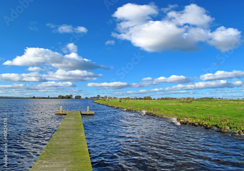 Sunny landscape in Holland, clear water with pier and meadow.