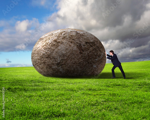 Businessman rolling a giant stone photo