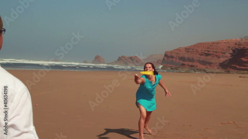 Happy couple having fun with freesby on the beach, slow motion photo