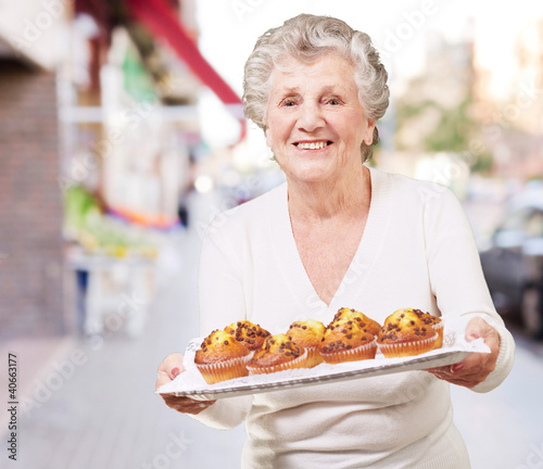 portrait of senior woman showing a chocolate muffin tray at stre