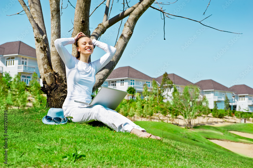 Fototapeta premium Pretty woman sitting by tree with laptop computer