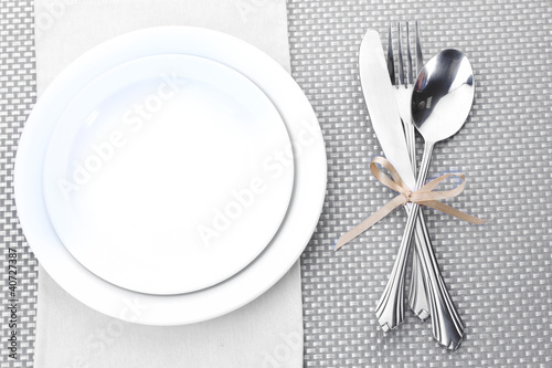 White empty plates with fork, spoon and knife tied with a ribbon