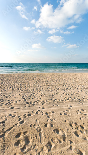 sandy beach with lots of footprints and a blue sky with clouds