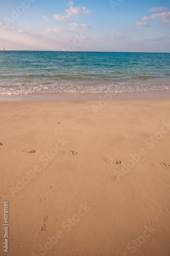sandy beach with lots of footprints and a blue sky with clouds