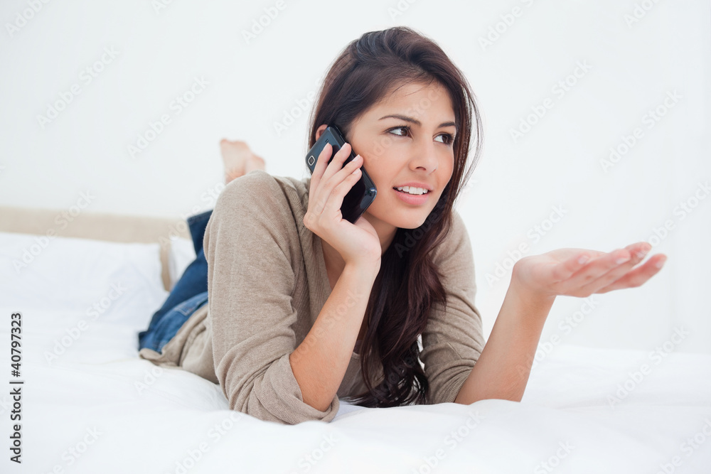 Woman making a phonecall glancing to the side as she lies on the Woman making a phonecall glancing to the side as she lies on the