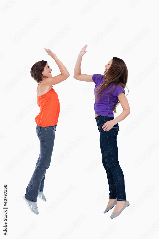 Two teenagers which are giving a high-five while jumping