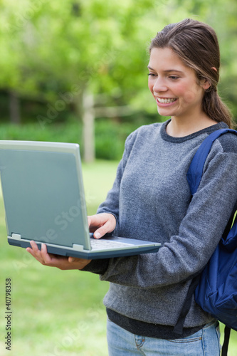 Happy student looking at the screen of her laptop while standing
