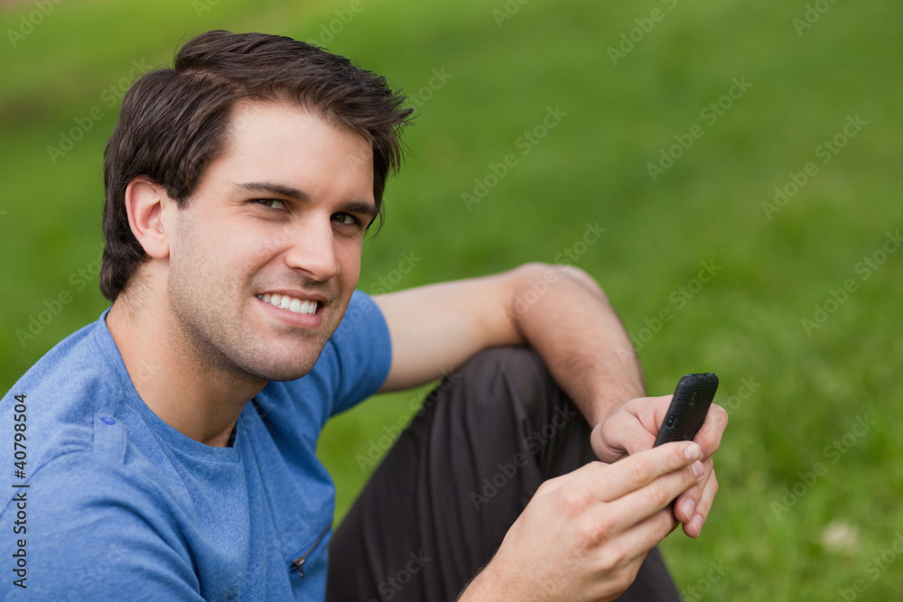 Happy young man looking at the camera while sending a text