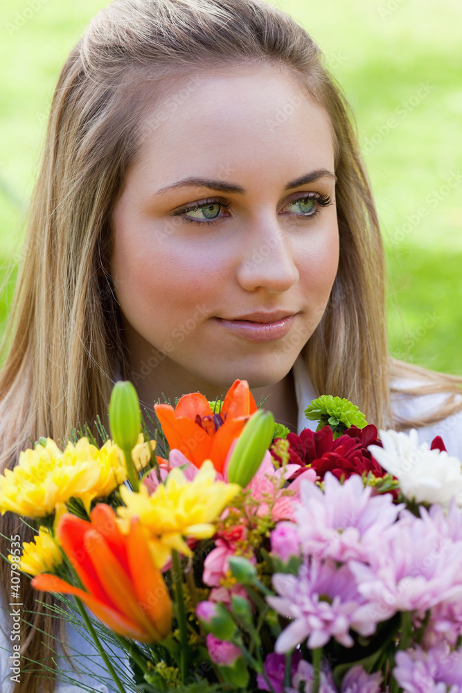 Young relaxed blonde girl holding a bunch of flowers while looki