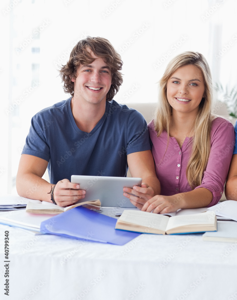 A couple hold a tablet together while looking into the camera A couple hold a tablet together while looking into the camera