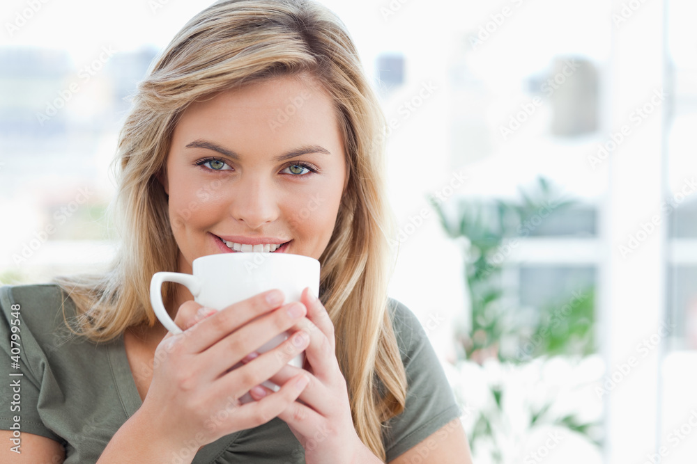 Woman looking forward, smiling with a mug up to near her mouth Woman looking forward, smiling with a mug up to near her mouth