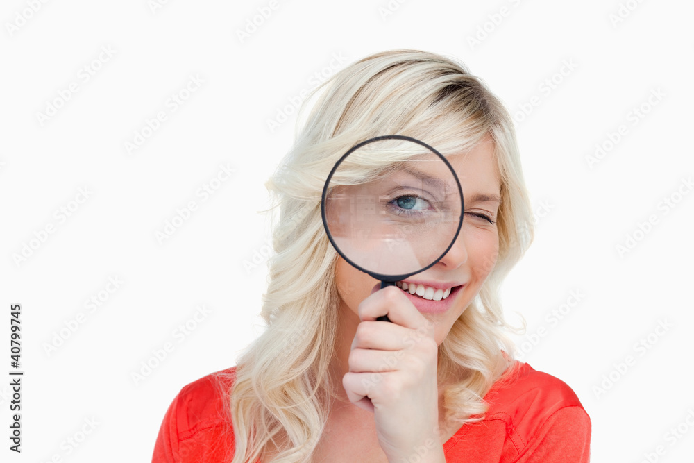 Woman looking through a magnifying glass while blinking an eye Woman looking through a magnifying glass while blinking an eye
