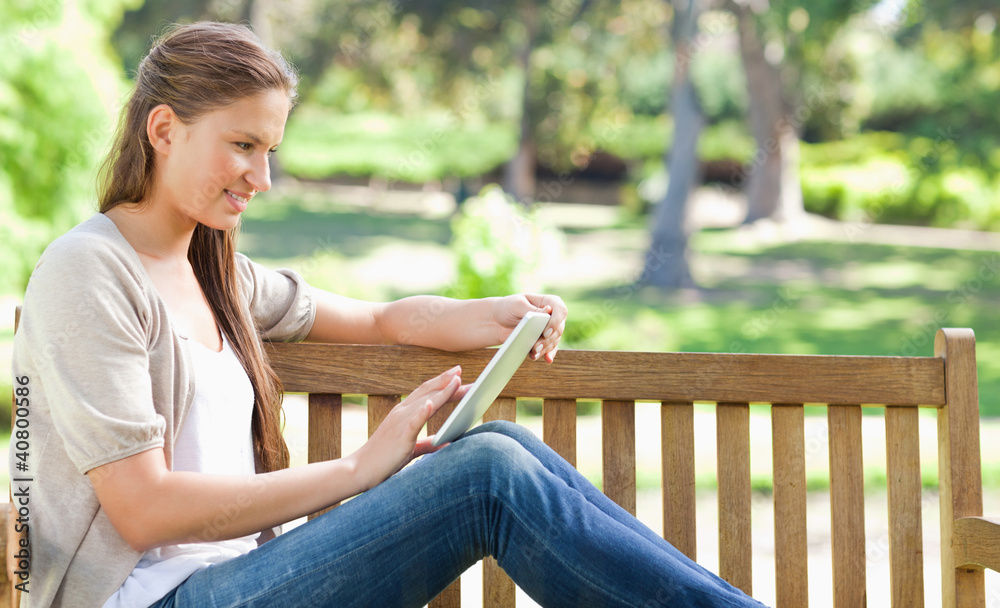Obraz premium Side view of a woman using a tablet computer on a park bench