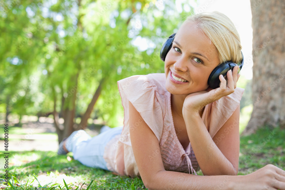 Smiling woman lying on the lawn while wearing headphones Smiling woman lying on the lawn while wearing headphones