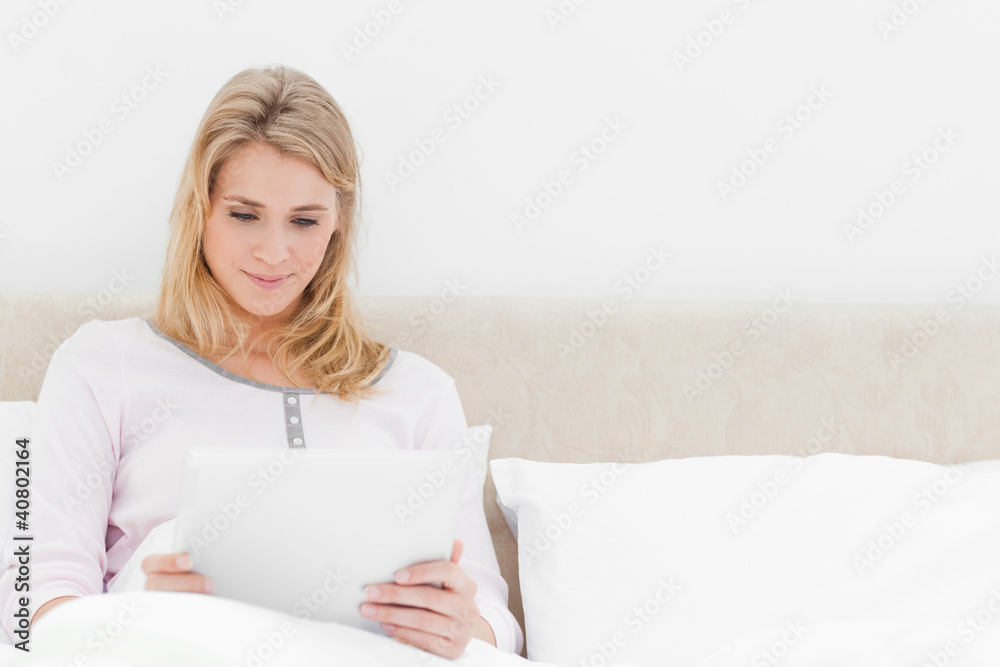 Woman sitting in bed, holding and watching a tablet pc Woman sitting in bed, holding and watching a tablet pc