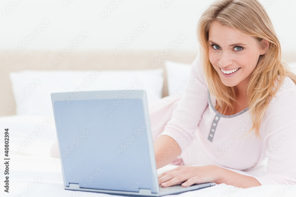Woman lying on the bed, with laptop, looking forward and smiling Woman lying on the bed, with laptop, looking forward and smiling