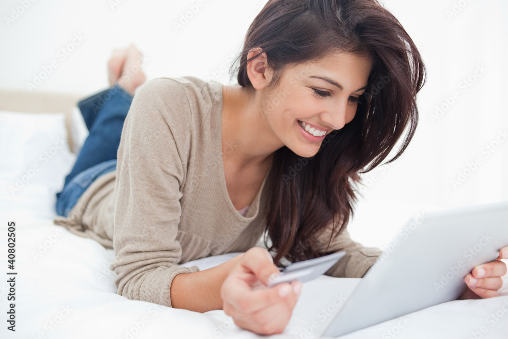 Woman using a tablet with her credit card, and smiling while lyi Woman using a tablet with her credit card, and smiling while lyi