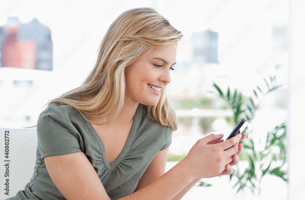 Woman smiles as she uses her phone while on the couch Woman smiles as she uses her phone while on the couch